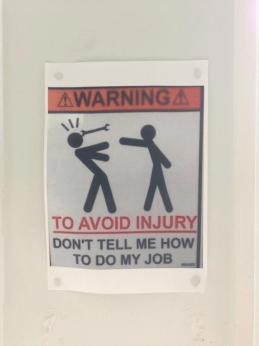 Skilt med stick figures og teksten: Warning! To avoid injury, don't tell me how to do my job
