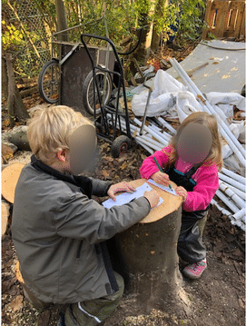 To børn står ved en træstub og skriver på papir